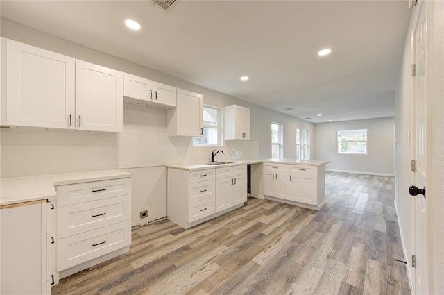 kitchen with light hardwood / wood-style floors, kitchen peninsula, white cabinetry, and a wealth of natural light