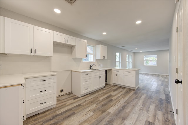 kitchen with sink, kitchen peninsula, tasteful backsplash, white cabinetry, and light wood-type flooring