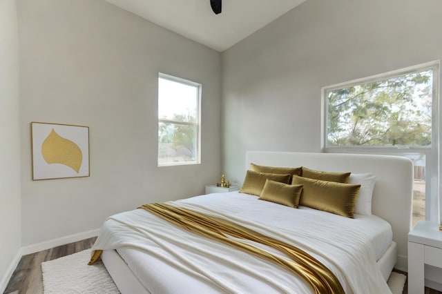 bedroom with multiple windows, ceiling fan, vaulted ceiling, and wood-type flooring