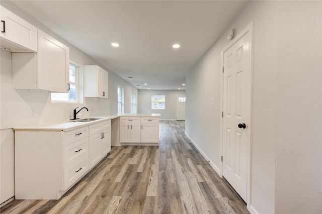 kitchen featuring tasteful backsplash, sink, kitchen peninsula, white cabinetry, and light hardwood / wood-style flooring