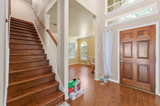 entrance foyer featuring a wealth of natural light, wood-type flooring, and crown molding