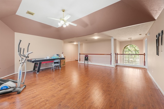 exercise room with wood-type flooring, a textured ceiling, vaulted ceiling, and ceiling fan