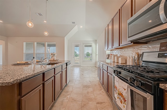 kitchen featuring stainless steel appliances, hanging light fixtures, sink, tasteful backsplash, and a kitchen island with sink