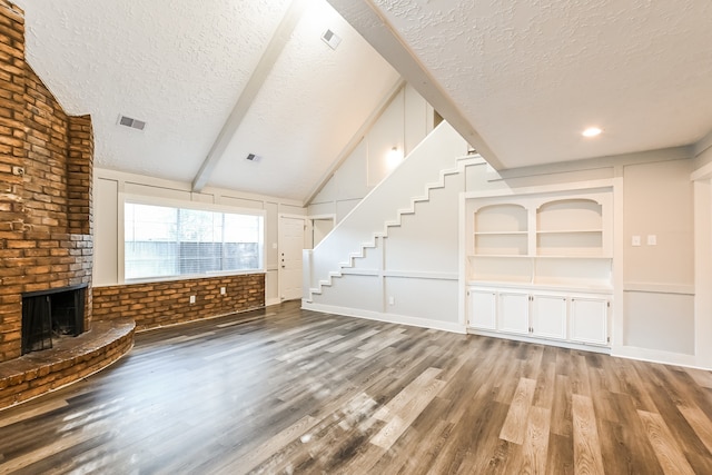 unfurnished living room featuring a textured ceiling, vaulted ceiling with beams, hardwood / wood-style floors, and a brick fireplace