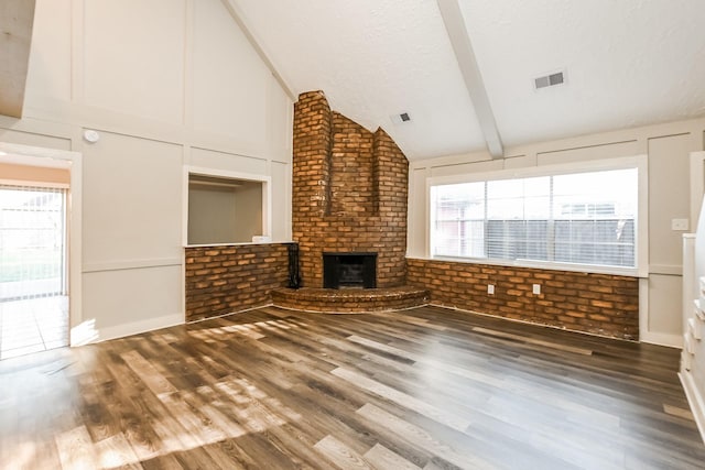 unfurnished living room featuring vaulted ceiling, a textured ceiling, visible vents, a brick fireplace, and wood finished floors