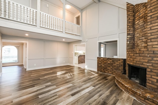 unfurnished living room with a decorative wall, wood finished floors, a towering ceiling, and a fireplace