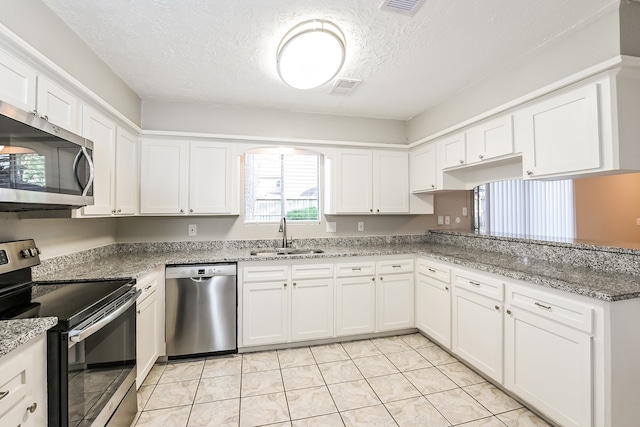 kitchen with light stone counters, a textured ceiling, sink, white cabinetry, and appliances with stainless steel finishes