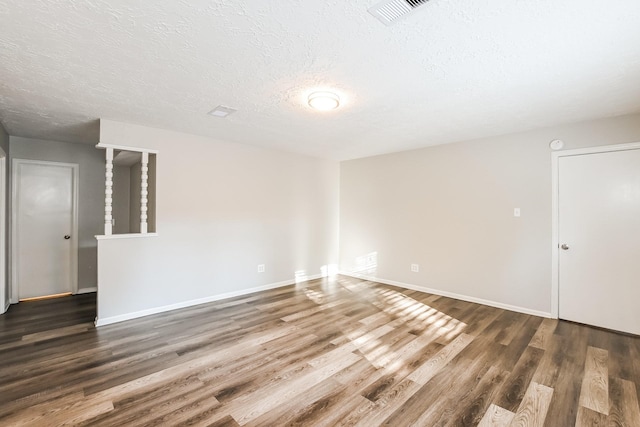 spare room featuring visible vents, a textured ceiling, baseboards, and wood finished floors