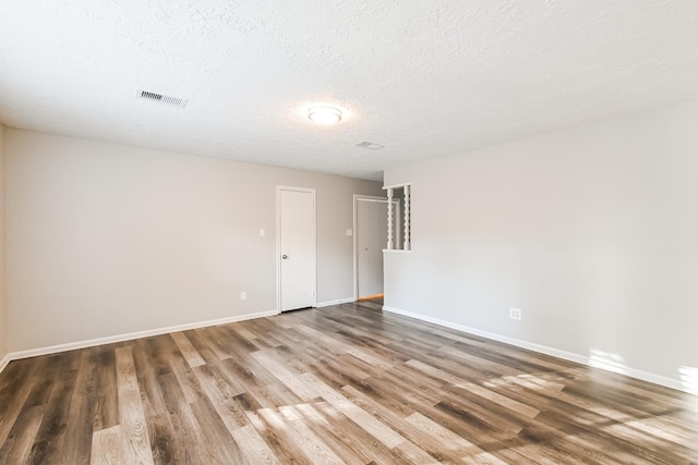 spare room featuring visible vents, baseboards, a textured ceiling, and wood finished floors