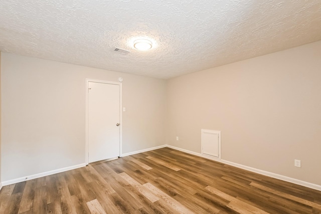 empty room featuring visible vents, baseboards, a textured ceiling, and wood finished floors