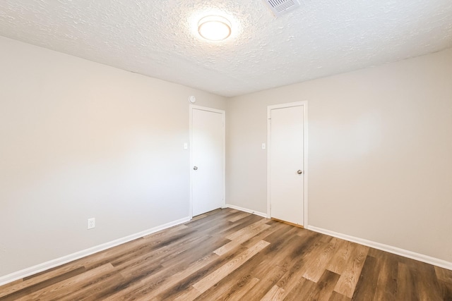 empty room featuring a textured ceiling, wood finished floors, baseboards, and visible vents
