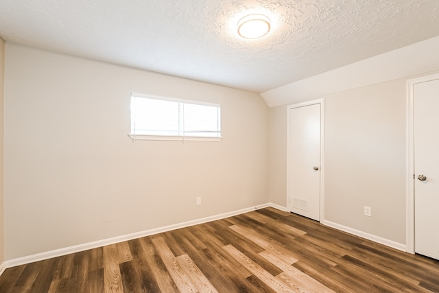 unfurnished room with a textured ceiling, vaulted ceiling, and dark wood-type flooring