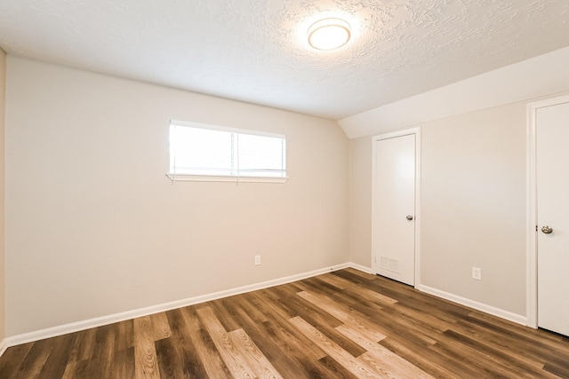 empty room featuring a textured ceiling, wood finished floors, and baseboards