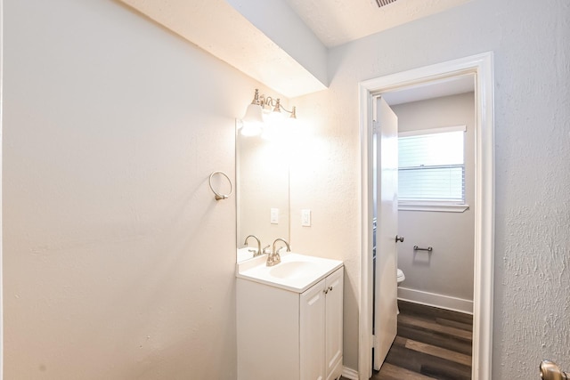bathroom with toilet, vanity, wood finished floors, and baseboards