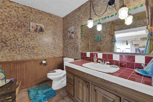 bathroom featuring tile patterned flooring, wood walls, vanity, and toilet