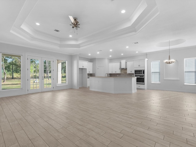 unfurnished living room with a raised ceiling, crown molding, light hardwood / wood-style floors, and ceiling fan with notable chandelier