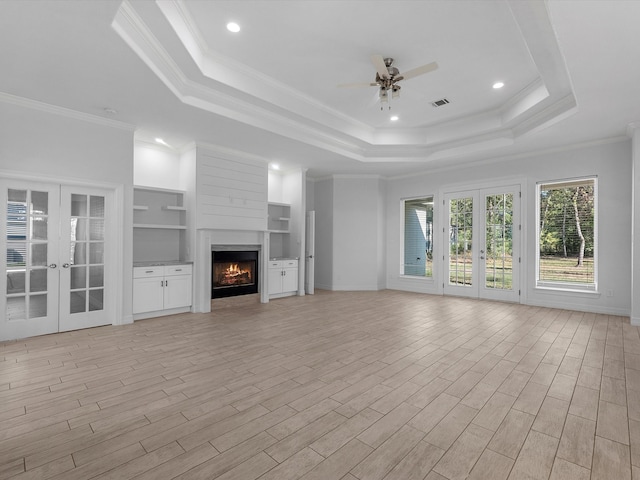 unfurnished living room featuring a tray ceiling, built in shelves, crown molding, and french doors