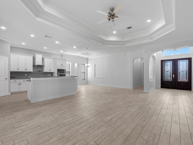 interior space with a tray ceiling, light wood-type flooring, ceiling fan with notable chandelier, and ornamental molding