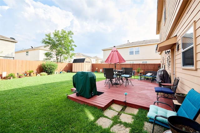 wooden terrace with a storage unit, a fenced backyard, an outbuilding, outdoor dining area, and a lawn