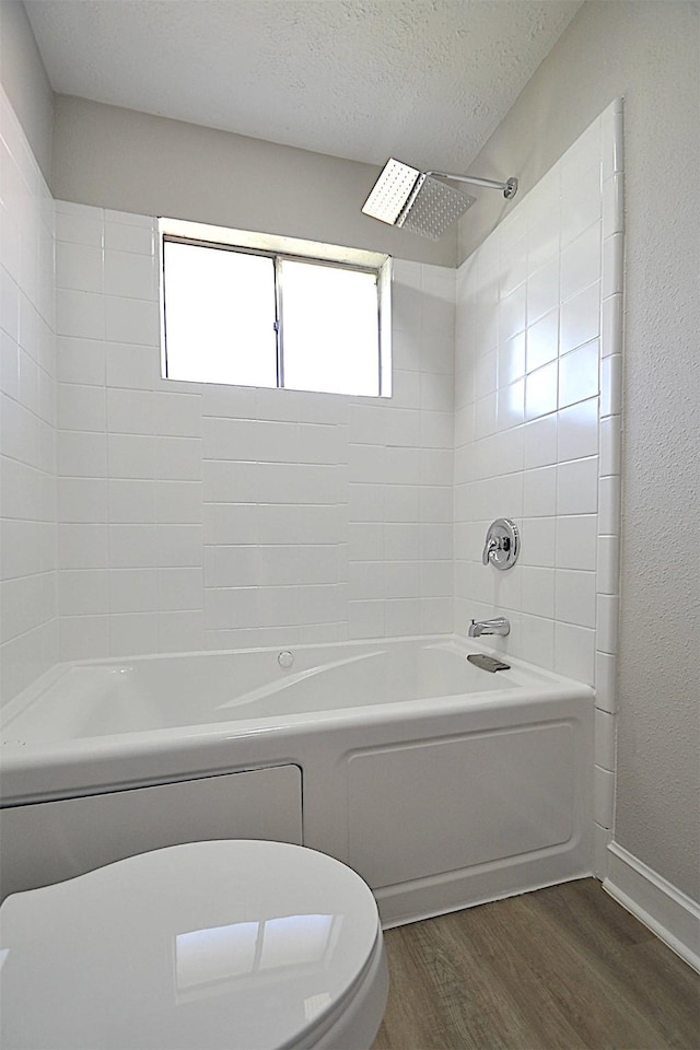 bathroom featuring tiled shower / bath combo, toilet, wood-type flooring, and a textured ceiling