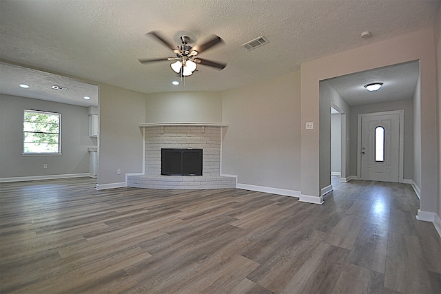 unfurnished living room featuring hardwood / wood-style floors, a fireplace, ceiling fan, and a textured ceiling