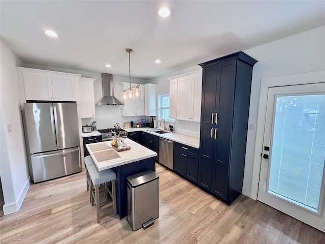 kitchen featuring appliances with stainless steel finishes, pendant lighting, a center island, sink, and wall chimney range hood