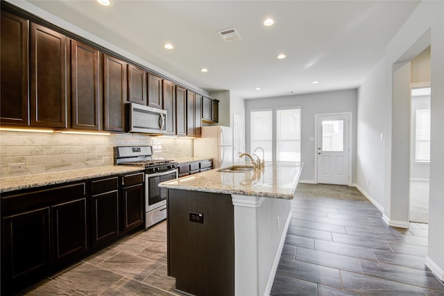 kitchen featuring light stone countertops, sink, backsplash, an island with sink, and appliances with stainless steel finishes