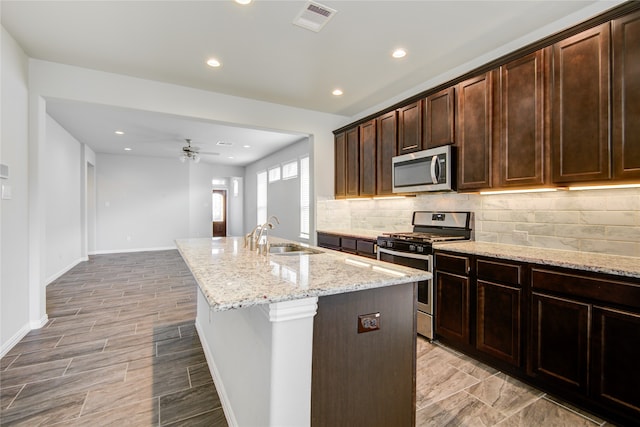 kitchen featuring light stone countertops, sink, an island with sink, decorative backsplash, and appliances with stainless steel finishes