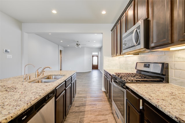 kitchen with dark brown cabinetry, sink, light stone counters, decorative backsplash, and appliances with stainless steel finishes