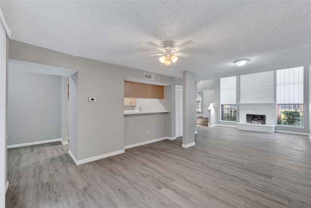 unfurnished living room with ceiling fan, light hardwood / wood-style floors, and a textured ceiling