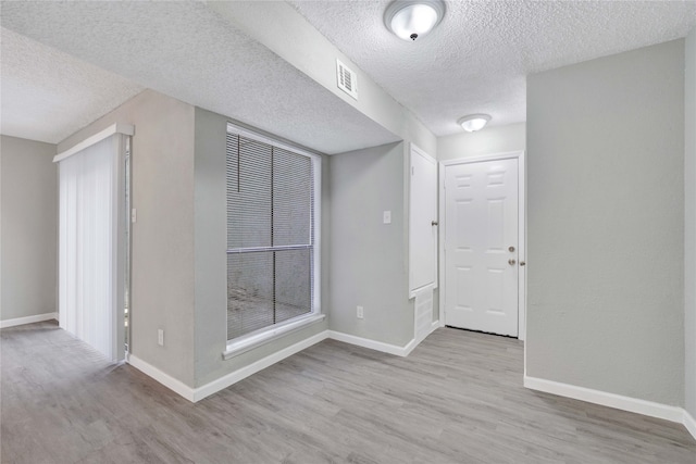 spare room featuring light wood-type flooring and a textured ceiling