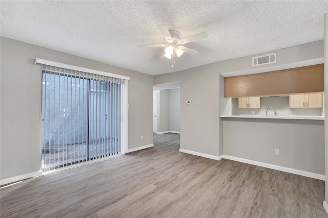 unfurnished living room featuring light hardwood / wood-style floors, sink, a textured ceiling, and ceiling fan