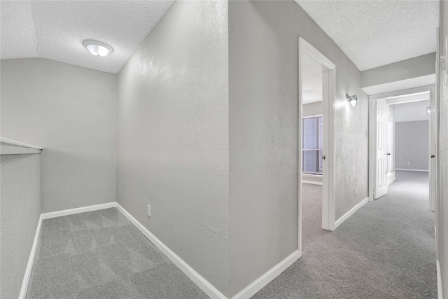 hall with lofted ceiling, carpet, and a textured ceiling