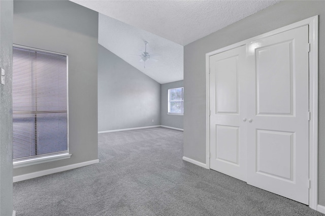 interior space with a textured ceiling, ceiling fan, vaulted ceiling, and carpet flooring