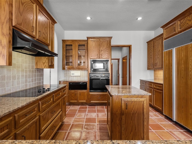 kitchen featuring tasteful backsplash, black appliances, light stone counters, and a center island