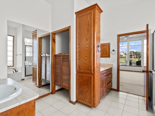 bathroom with tiled tub, vanity, ceiling fan, and tile patterned floors