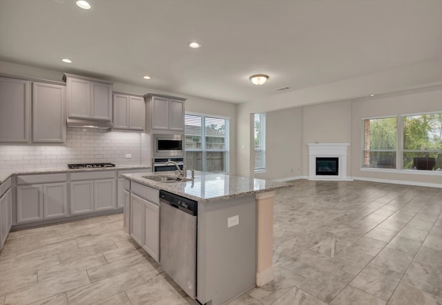 kitchen with gray cabinets, a kitchen island with sink, sink, appliances with stainless steel finishes, and light stone countertops