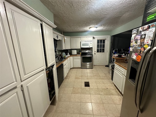 kitchen with light tile patterned flooring, white cabinetry, stainless steel appliances, and a textured ceiling