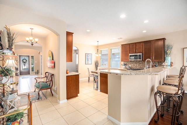 kitchen featuring a breakfast bar area, light stone countertops, decorative backsplash, kitchen peninsula, and hanging light fixtures