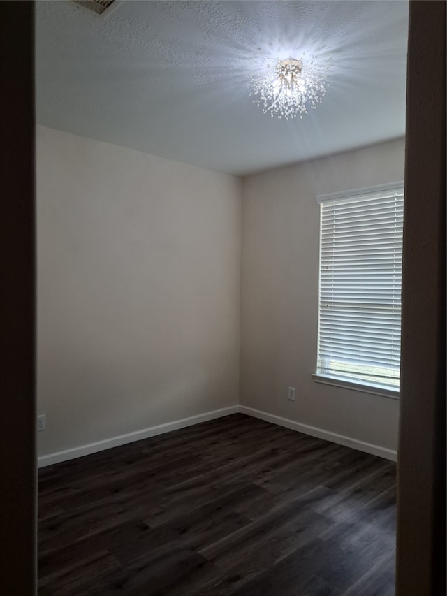 unfurnished room featuring a chandelier and dark wood-type flooring