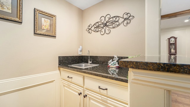 bar featuring dark stone counters, hardwood / wood-style floors, cream cabinets, and sink