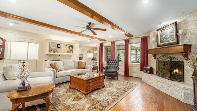 living room featuring wood-type flooring, beam ceiling, a fireplace, ornamental molding, and ceiling fan