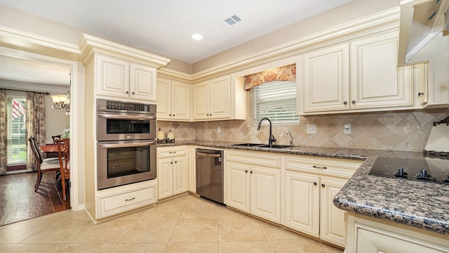 kitchen featuring appliances with stainless steel finishes, cream cabinetry, dark stone countertops, decorative backsplash, and sink