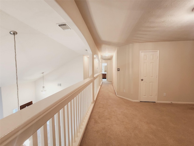 corridor with a textured ceiling, lofted ceiling, and light carpet