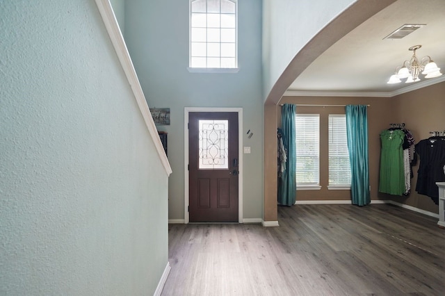 foyer entrance featuring wood-type flooring, ornamental molding, and a chandelier