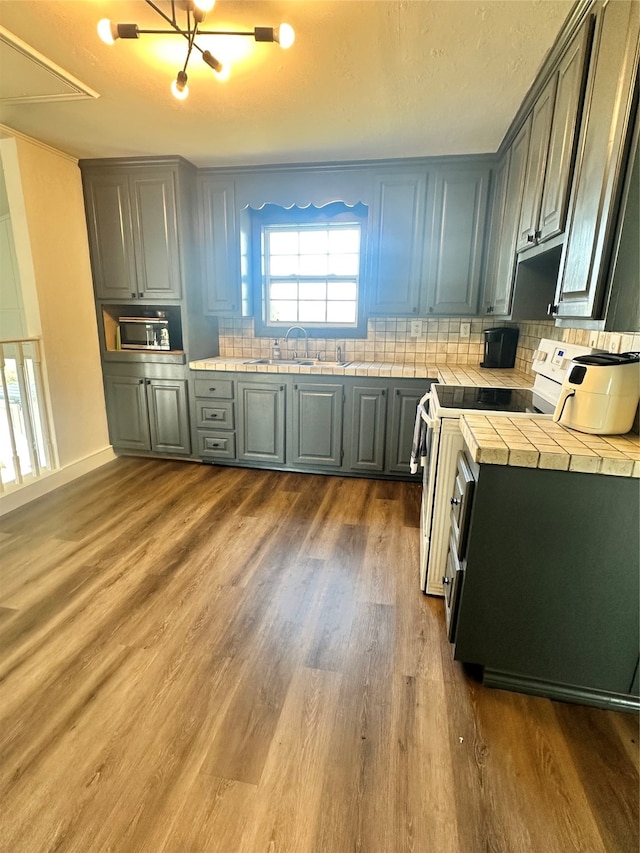 kitchen featuring decorative backsplash, tile counters, dark wood-type flooring, sink, and range