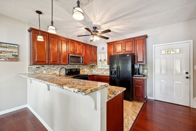 kitchen featuring wood-type flooring, a textured ceiling, kitchen peninsula, black appliances, and decorative light fixtures