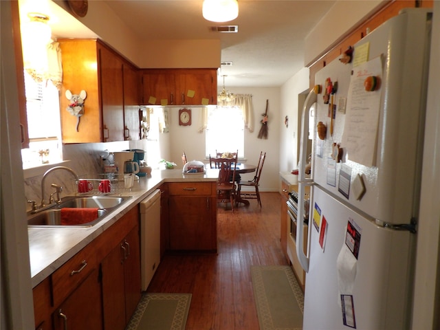 kitchen featuring hanging light fixtures, kitchen peninsula, sink, white appliances, and dark hardwood / wood-style flooring