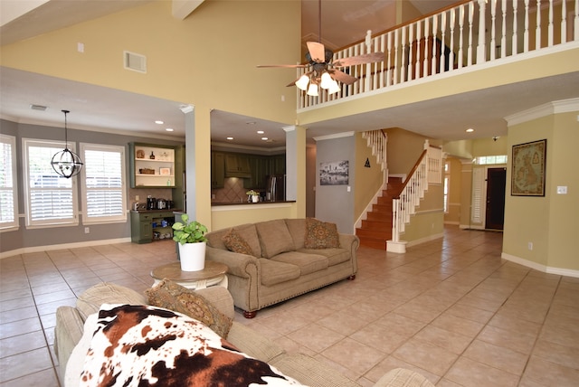 tiled living room with ceiling fan with notable chandelier, decorative columns, ornamental molding, and high vaulted ceiling