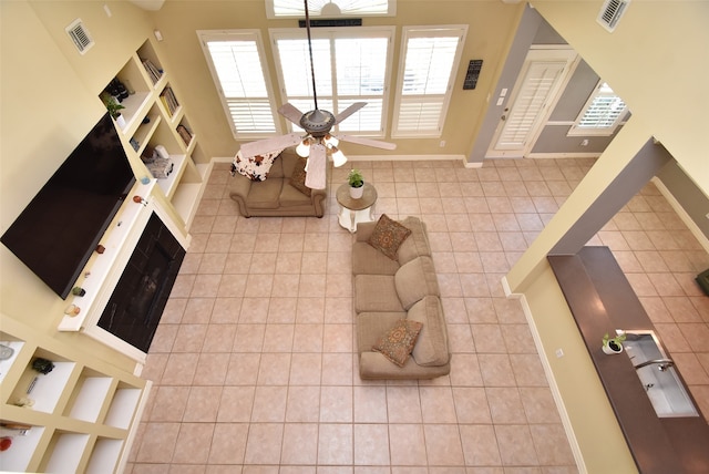 tiled living room with built in shelves, a fireplace, a towering ceiling, and ceiling fan